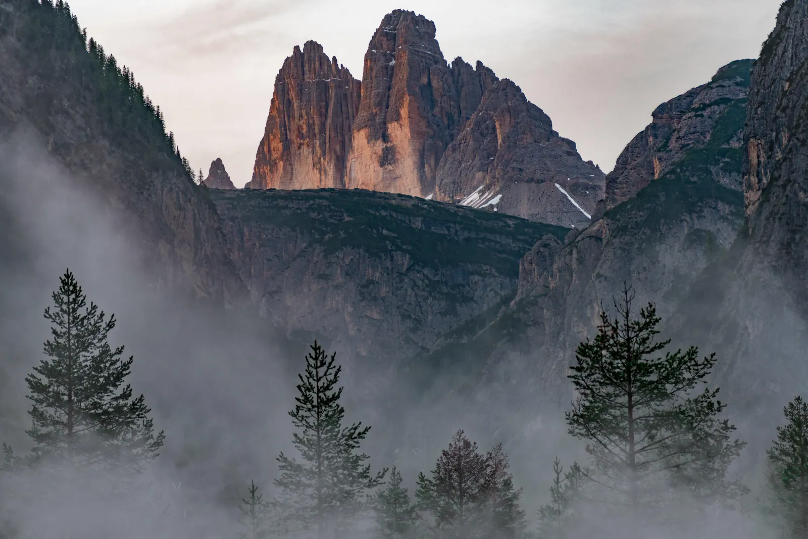 Tre Cime di Lavaredo rising above the misty forest