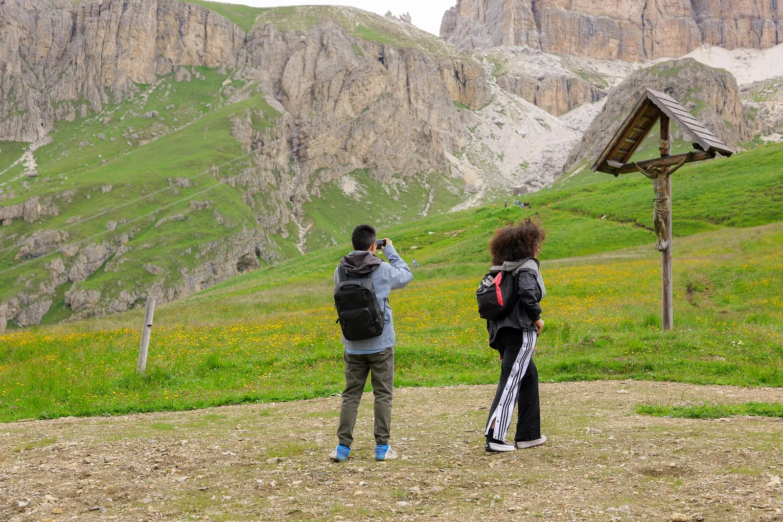 Hikers by a wooden wayside cross on the meadows below the Sella towers